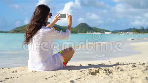 年轻女子躺在白色的沙滩上通过电话交谈视频的预览图