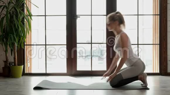 年轻漂亮的运动女性金发碧眼穿着白色运动服在灰色的地毯上做瑜伽和伸展运动视频的预览图