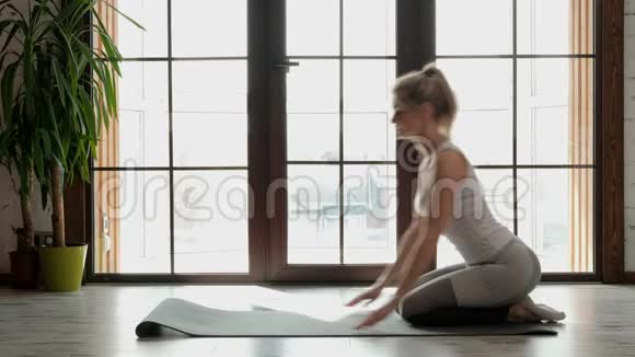 年轻漂亮的运动女性金发碧眼穿着白色运动服在灰色的地毯上做瑜伽和伸展运动视频的预览图