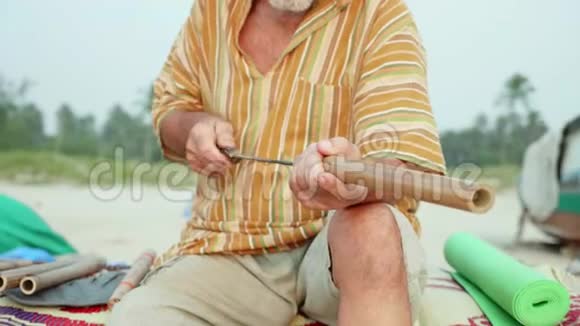 老人坐在海滩上用手制作长笛特写视频的预览图