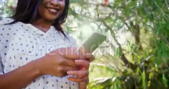女人的肖像正在使用智能手机在花园里微笑视频的预览图