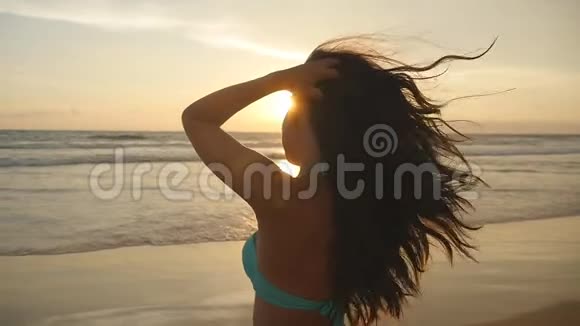 美丽的女孩长发在日出时摆在海边穿比基尼的漂亮年轻女子站着视频的预览图