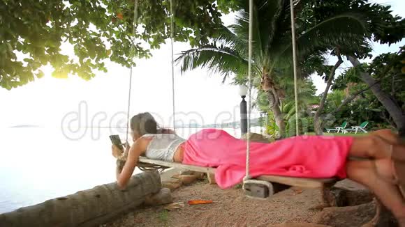 女人躺在棕榈树的秋千上用智能手机视频的预览图