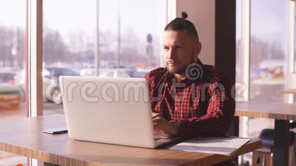 一个留胡子的嬉皮士在咖啡馆的笔记本电脑里工作视频的预览图