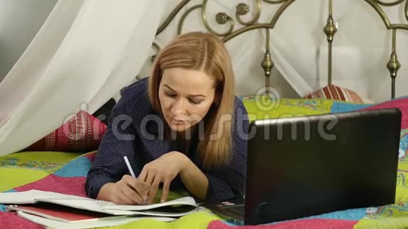 漂亮的女人在她房间里的一张床上学习笔记本电脑网上教育视频的预览图