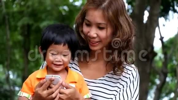 一个亚裔男孩和母亲正在公园玩智能手机游戏视频的预览图