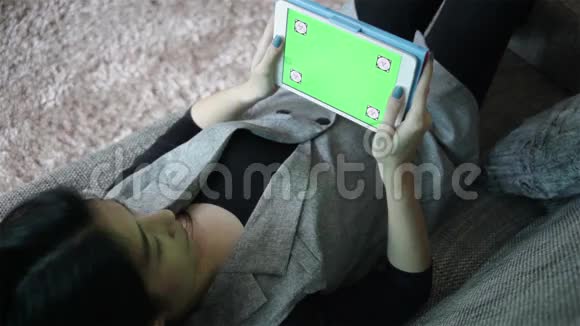 商务女性和带绿色屏幕的数字平板电脑躺在沙发上在办公室工作全高清视频的预览图