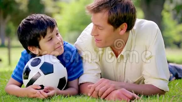 快乐的父子俩用足球躺在草地上视频的预览图