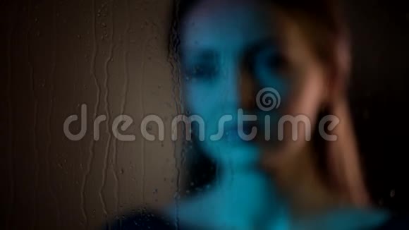 忧伤梦幻迷人的白种人年轻女子望着热气腾腾的玻璃窗在夜色中触摸着手掌蓝色的霓虹灯视频的预览图