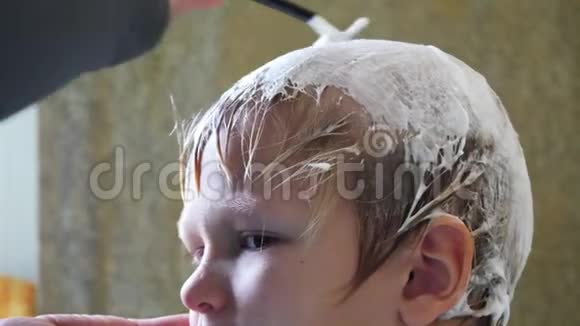 年轻的母亲用剃刀剃掉金发男孩的头以防止椎弓根良好的家庭传统视频的预览图