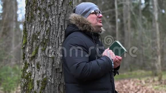 带着圣经和念珠在树旁祈祷的人视频的预览图