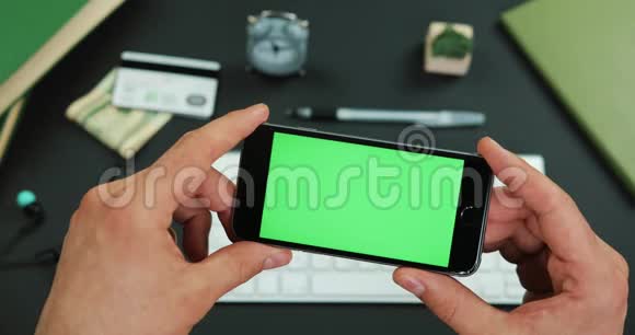 男人在工作桌上拿着绿色屏幕的智能手机视频的预览图