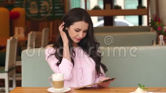 带着平板电脑和咖啡坐在咖啡馆里的年轻女孩视频的预览图