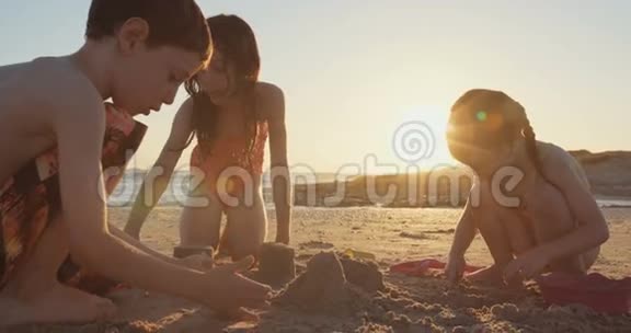 三个孩子在日落时在海滩上建造沙堡视频的预览图