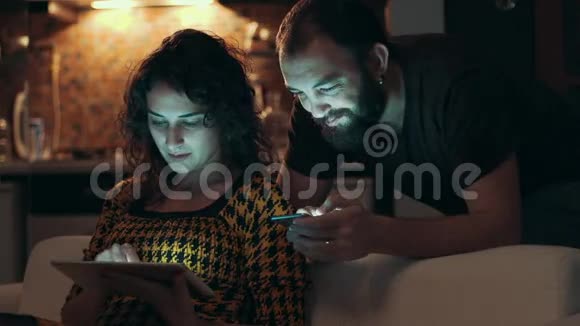 一对夫妇晚上在房间的沙发上用平板电脑视频的预览图