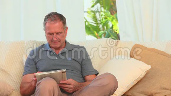 坐在沙发上拿着报纸的退休男子视频的预览图