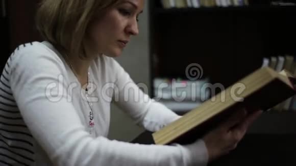 年轻女子在图书馆读一本大书有书的书架视频的预览图