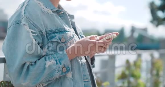阳光明媚的一天美丽的年轻女子穿着牛仔夹克在城市公园打电话视频的预览图