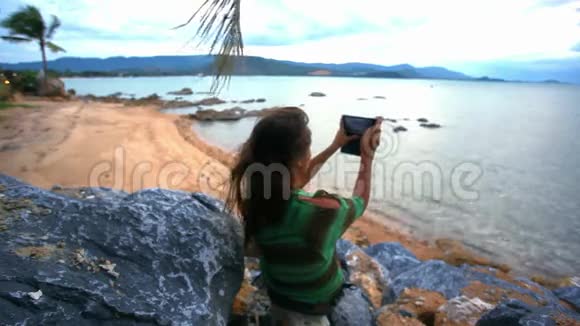 年轻女子在岩石上通过电话拍照视频的预览图