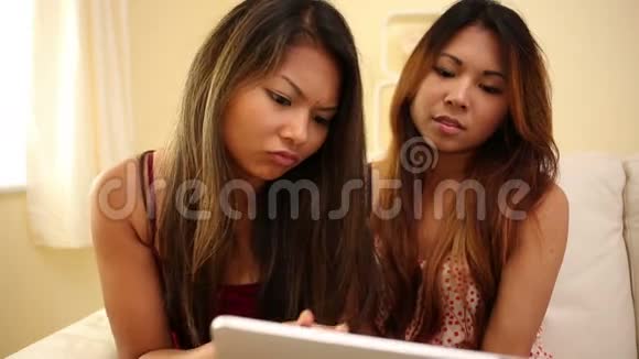 有魅力的姐妹用平板电脑坐在沙发上视频的预览图
