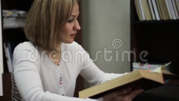 年轻女子在图书馆读一本大书有书的书架视频的预览图