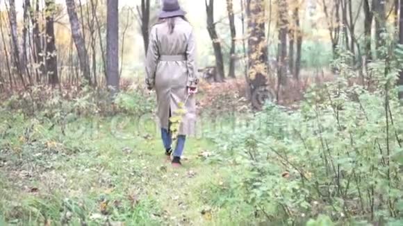 一个穿着雨衣和帽子的女人正在穿过秋天的森林视频的预览图