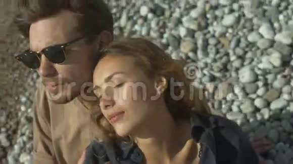 一对相爱的年轻夫妇坐在沙滩上视频的预览图