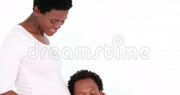 微笑的丈夫听着他怀孕的妻子的肚子视频的预览图