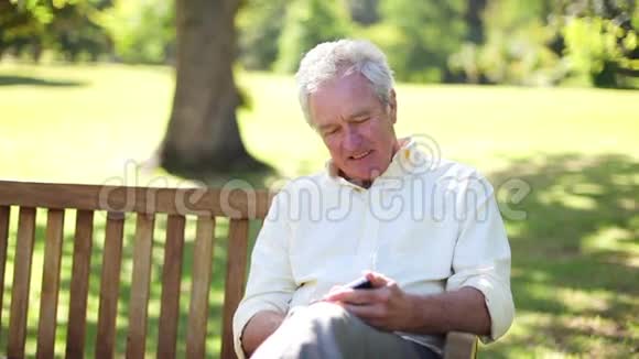 坐在长凳上用手机的退休男子视频的预览图