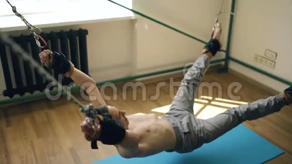 年轻男子在健身器材上游泳用绳子拉他的胳膊和腿视频的预览图