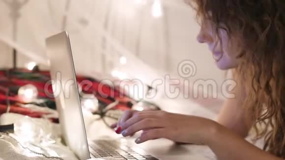 年轻女子躺在床上手提电脑放在花环背景上视频聊天网上购物视频的预览图