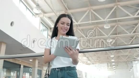 美丽的年轻女学生在购物中心使用她的白色平板电脑快乐的大学生活视频的预览图