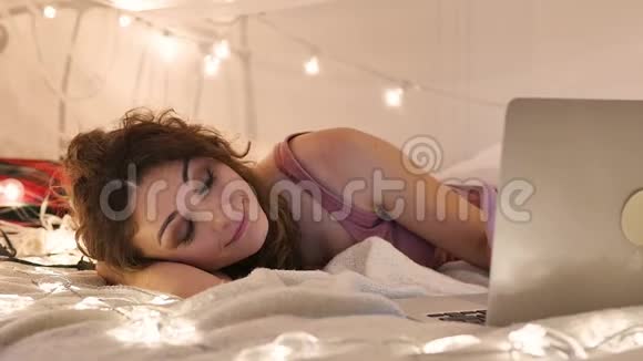 年轻女子躺在床上手提电脑放在花环背景上视频聊天网上购物视频的预览图