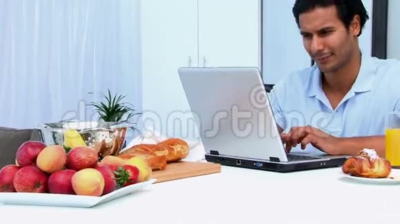 快乐的男人一边吃早餐一边用笔记本电脑视频的预览图
