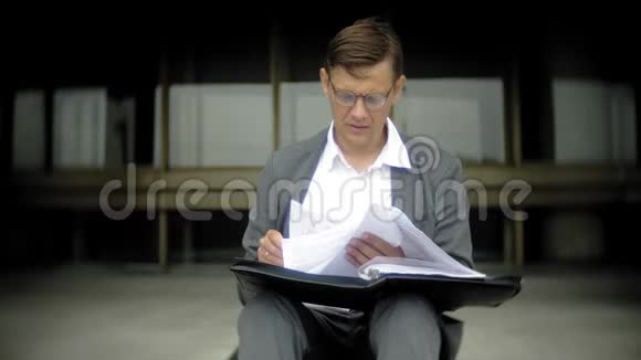 商人坐在城市的楼梯上他穿着西装和公文包他在看文件视频的预览图