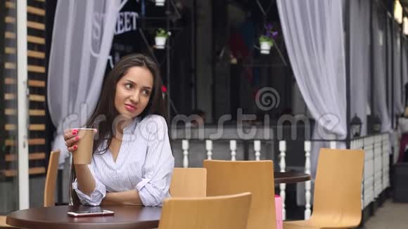 年轻女孩坐在街头咖啡馆里喝咖啡视频的预览图