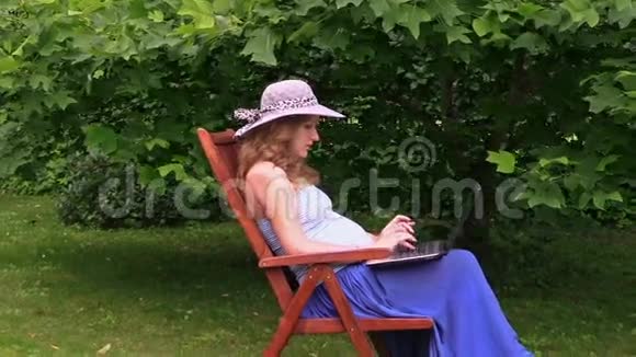 戴帽子的孕妇坐在木椅上工作手提电脑视频的预览图