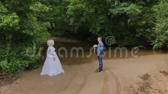 美丽的新郎和金发新娘在森林里的小溪旁视频的预览图