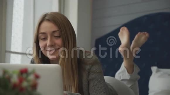 带着笔记本电脑躺在床上的微笑女孩视频的预览图