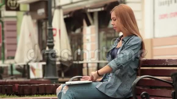 年轻时尚的女人带着笔记本电脑坐在长凳上工作视频的预览图