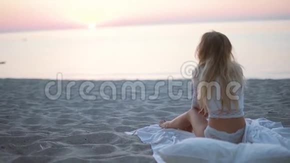 海滩上美丽的金发女孩看着大海和照相机在黄金时间被推在海滩上情绪化的脸视频的预览图
