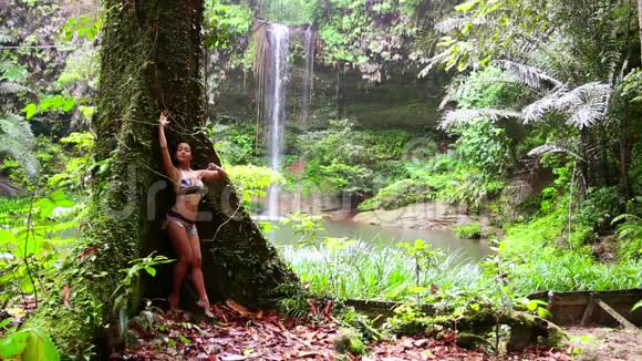热带雨林背景瀑布的女孩斜倚着大树视频的预览图