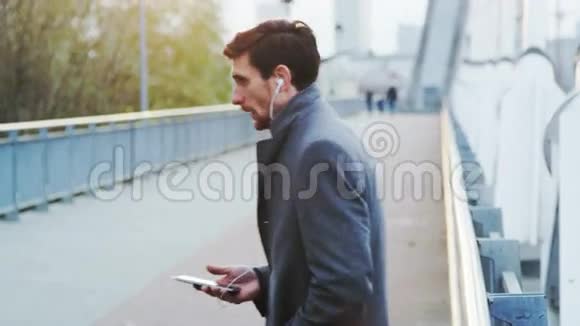 年轻的商人在户外一边用耳机一边打电话视频的预览图