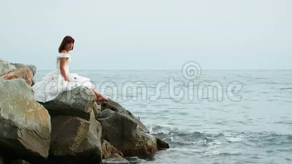 穿着白衣服坐在岩石旁的美丽女人视频的预览图