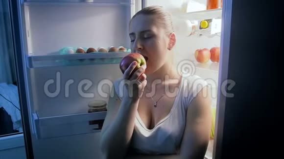 美丽的年轻女子晚上在厨房吃新鲜苹果视频的预览图