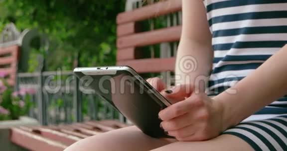 坐在长凳上的公园里有数字平板电脑的年轻女孩视频的预览图