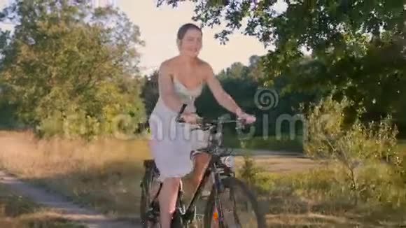 美丽的年轻女子骑着自行车在乡村夕阳下视频的预览图