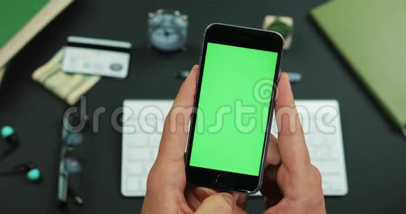 男人在工作桌上拿着绿色屏幕的智能手机视频的预览图