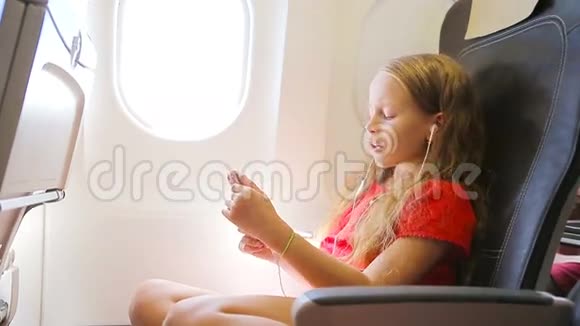 可爱的小女孩乘飞机旅行小孩坐在飞机窗前听音乐视频的预览图
