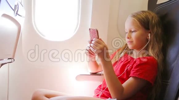 可爱的小女孩坐在靠窗的飞机上小孩坐在飞机窗前听音乐视频的预览图